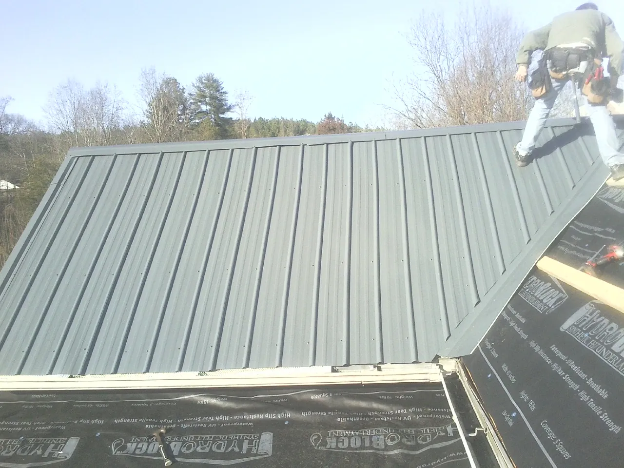 Crew installing dark green standing seam panels over synthetic underlayment in Portola Valley