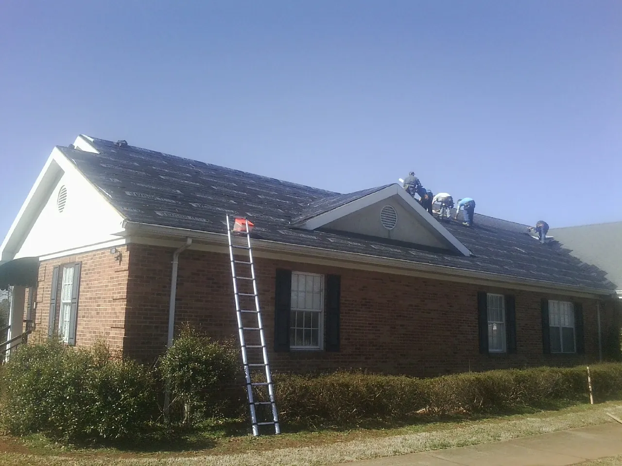 Crew tearing shingles off a brick ranch roof with a ladder set — Emergency Roof Repair work by our crew in Portola Valley