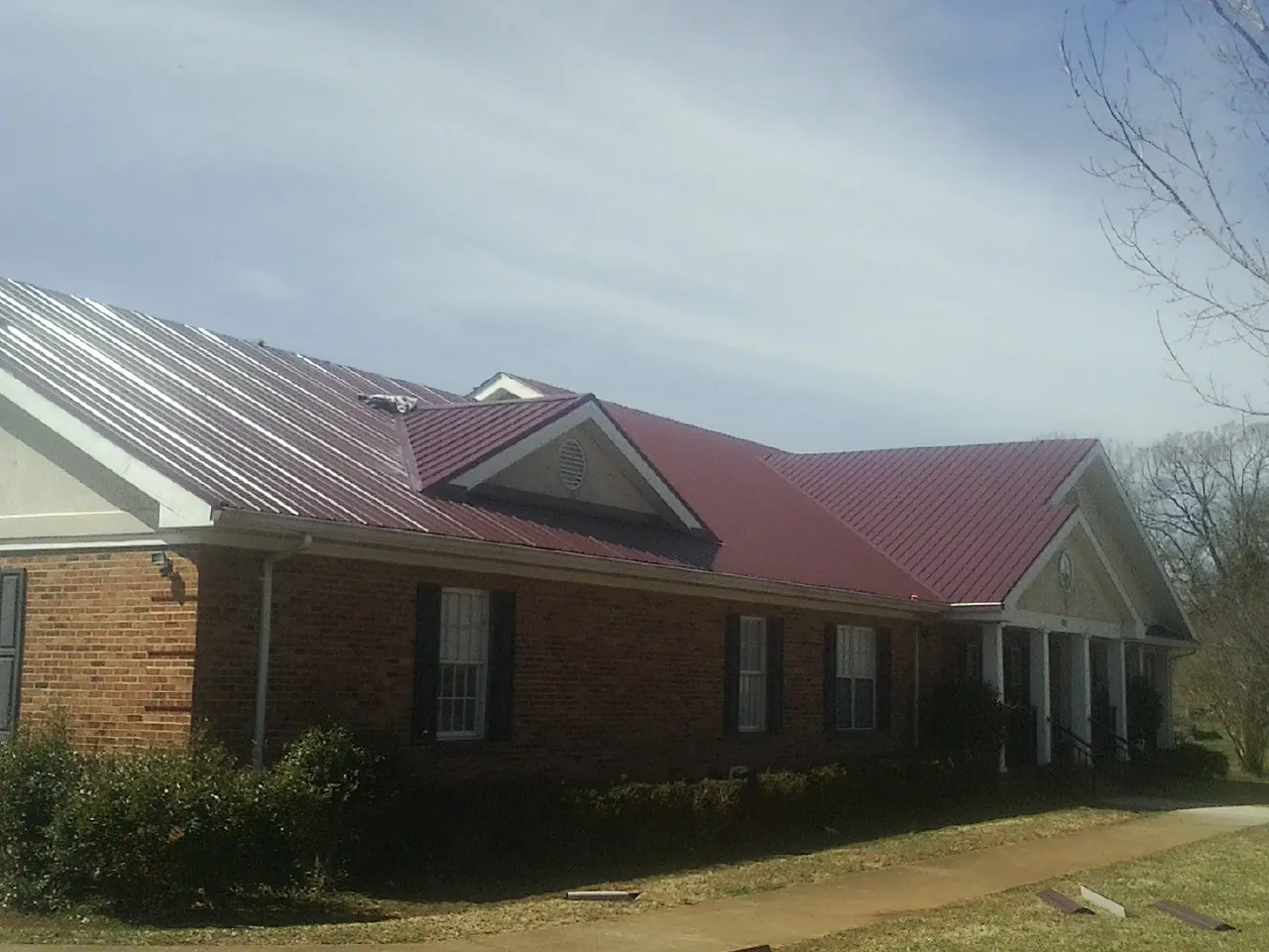 Red metal roof with gabled entries on a long brick building, from a Hail Damage Roof Repair job in Portola Valley