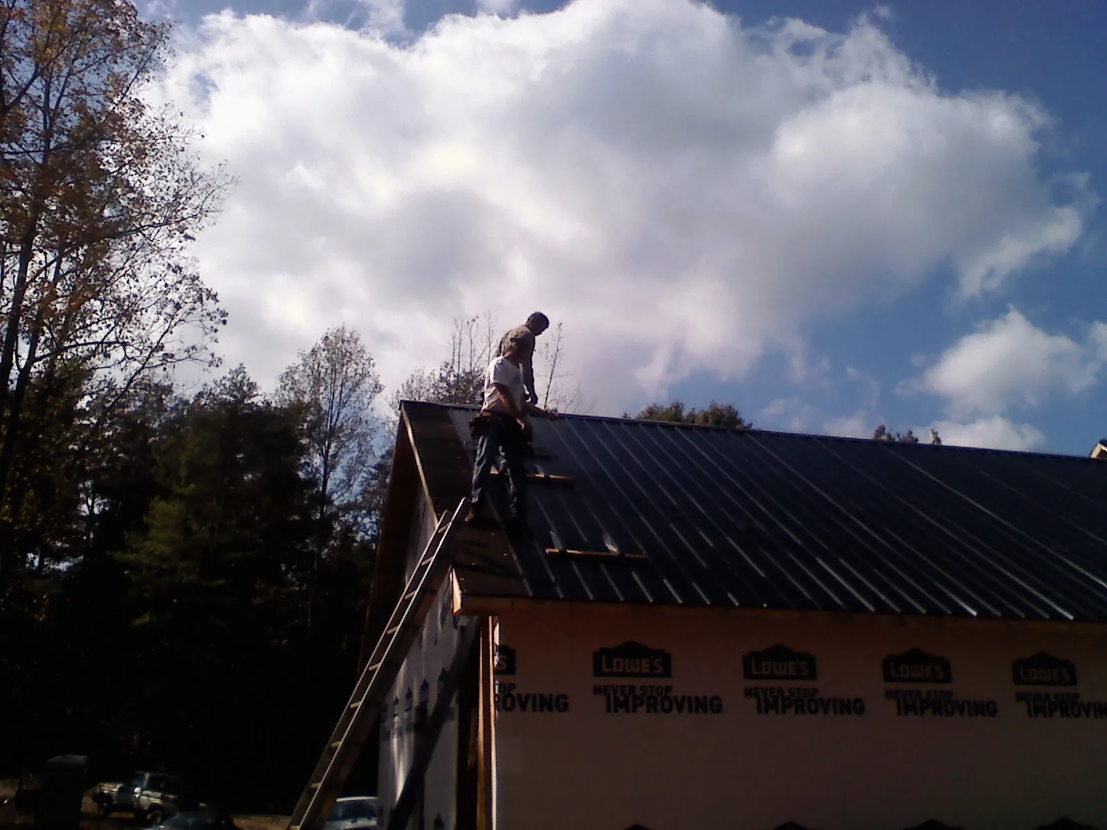 Roofer fastening dark metal panels high against a cloudy sky, from a Roof Inspection job in Portola Valley