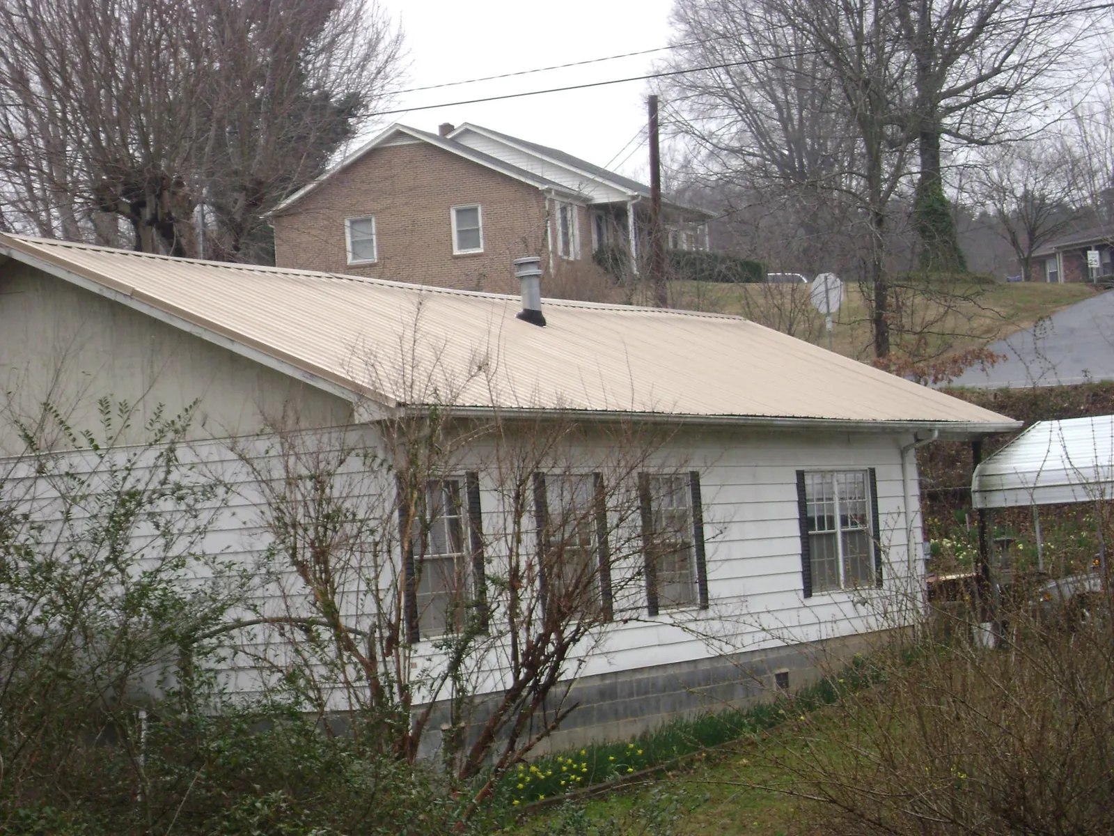 Tan metal roof on a white sided house set into a hillside — Commercial Roofing by Roofing Brothers in Portola Valley